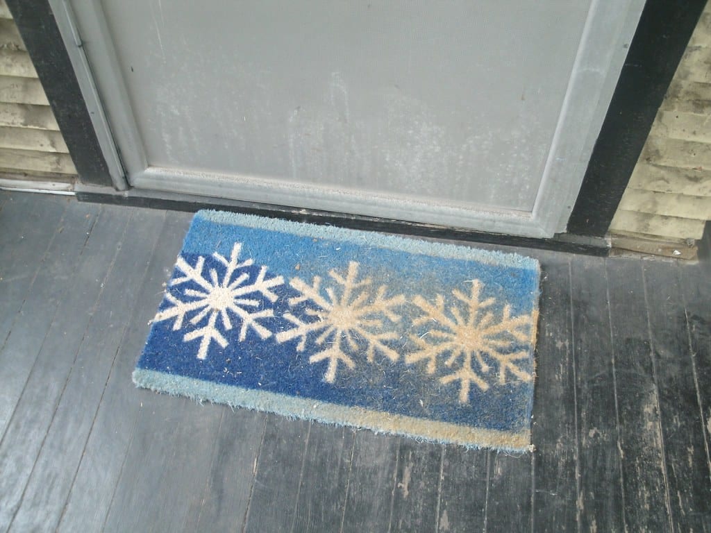 An exterior door bottom and threshold with a winter doormat in front