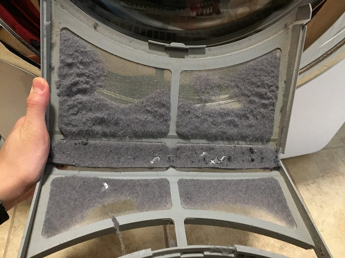 A dryer lint trap opened with thick gray lint clogging the screen