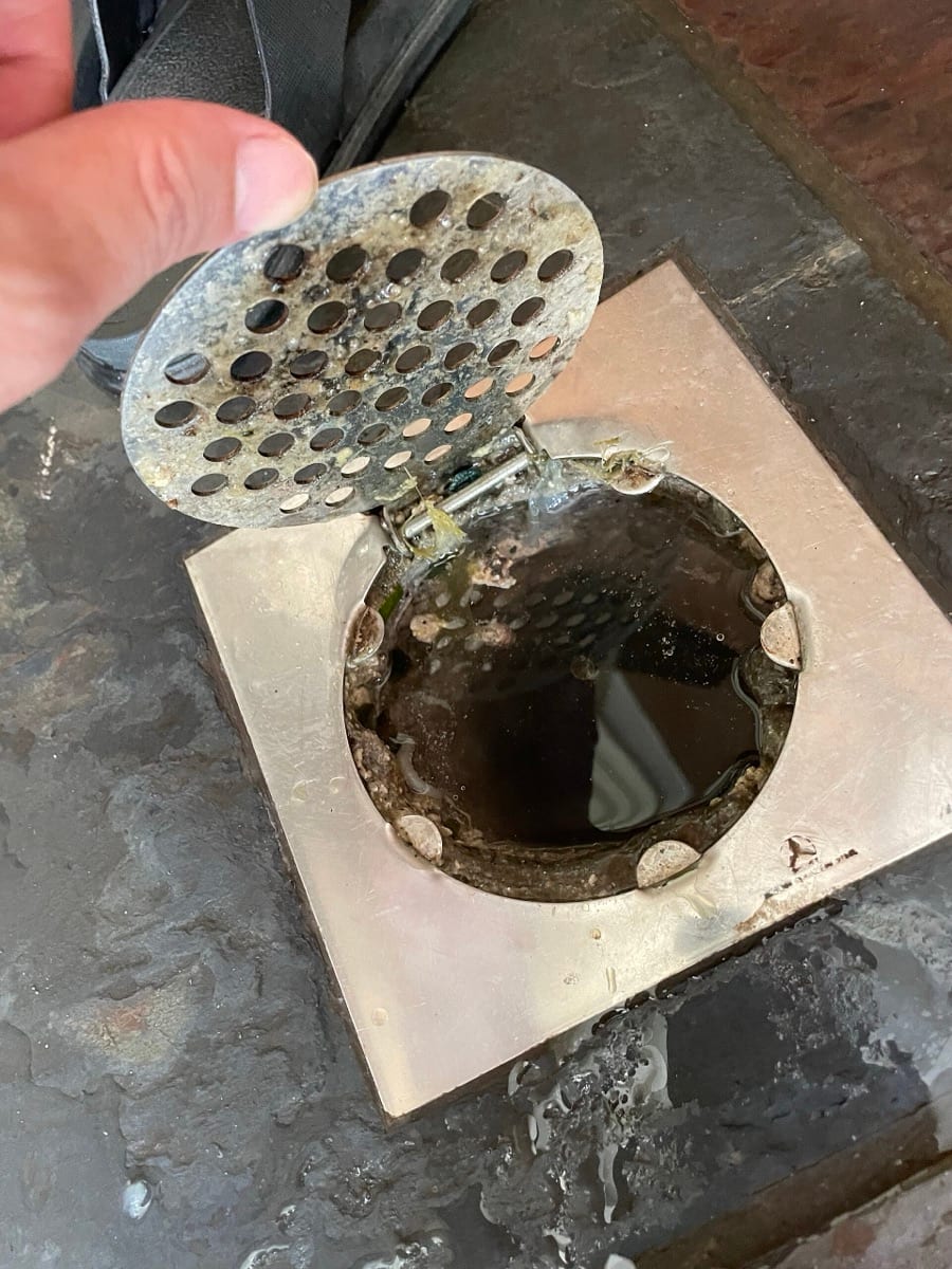 A floor drain with the grate lifted, showing the dirty opening beneath