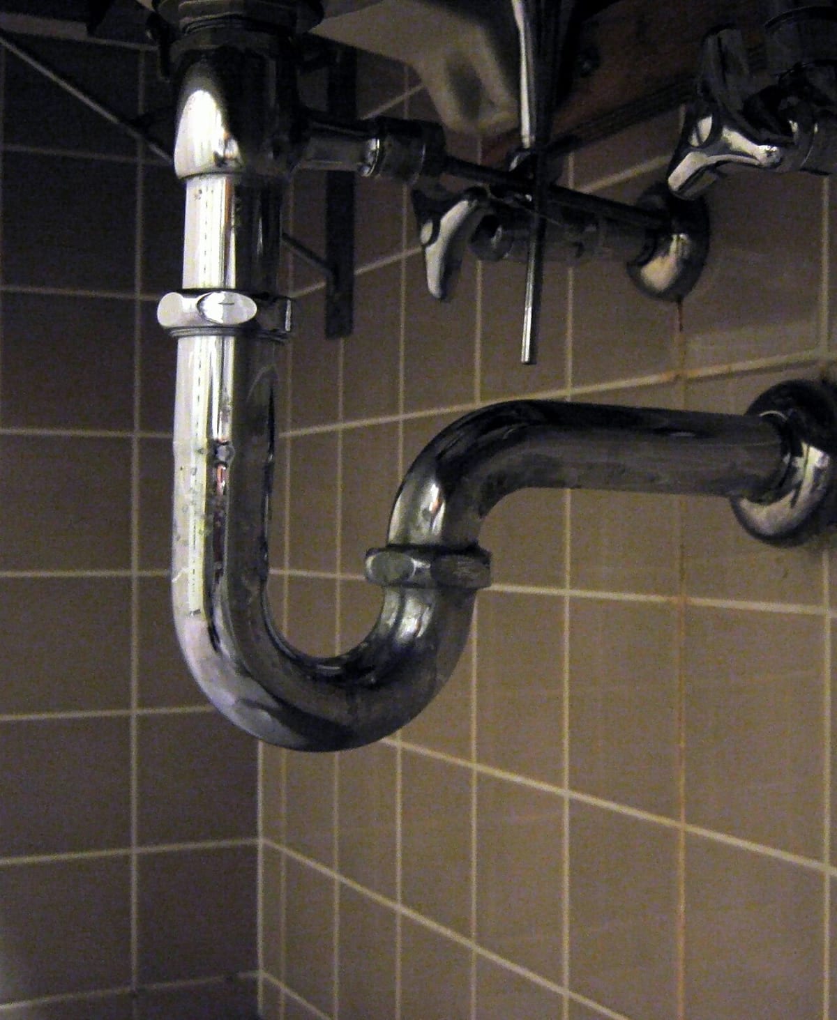 A chrome P-trap under a sink with its tailpiece, two slip nuts, and the trap arm running into the wall