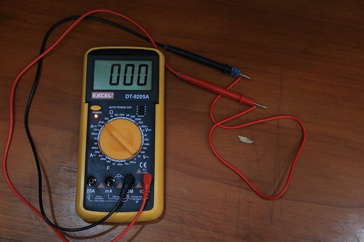 A digital multimeter on a workbench with its red and black test probes