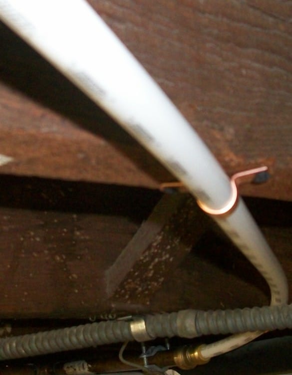 A white pipe held against a basement joist by a small copper pipe hook