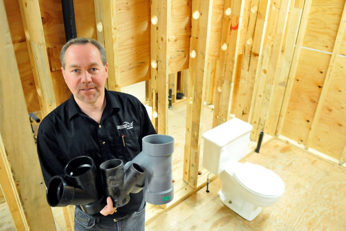 A plumber holding pipe fittings beside a newly installed toilet