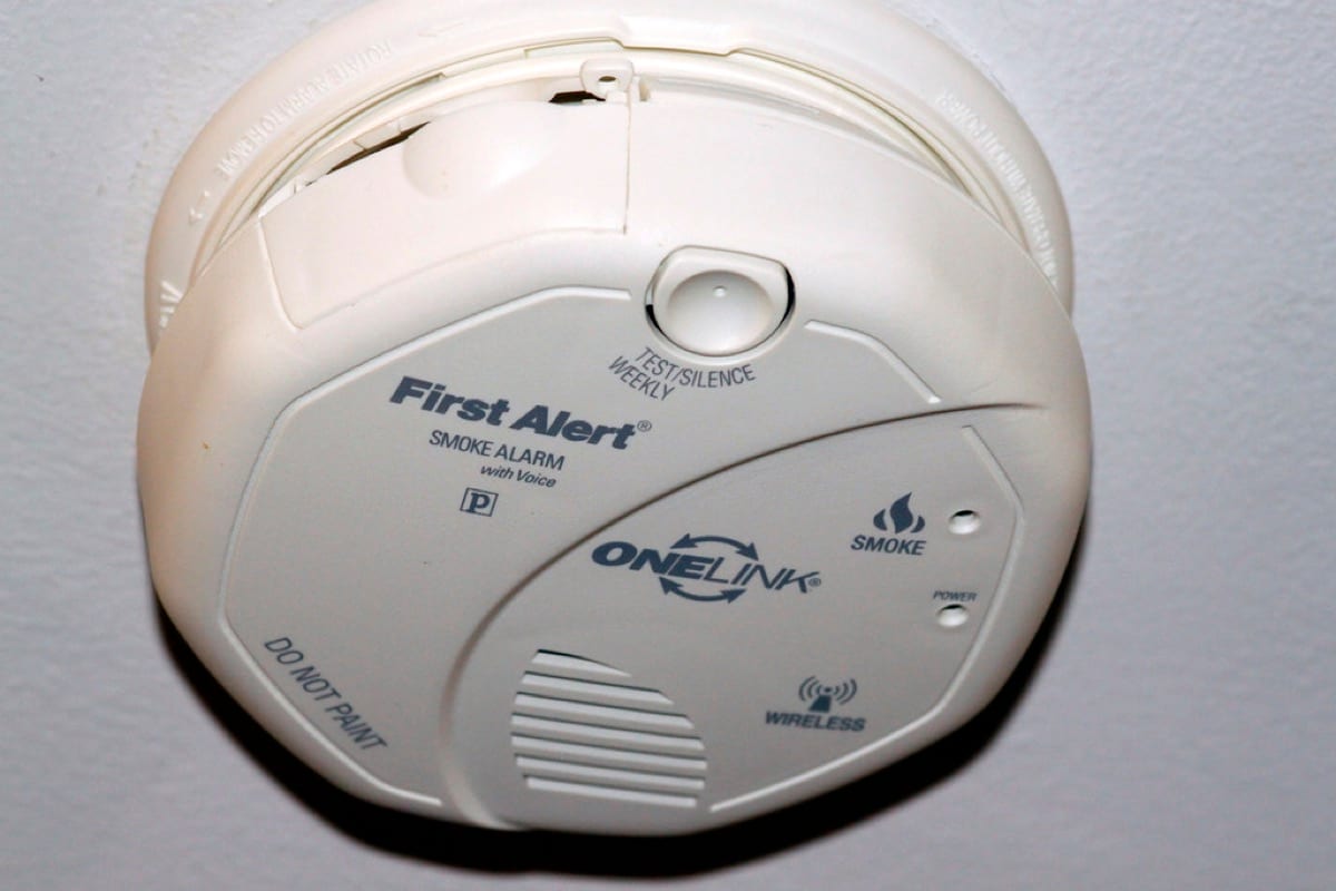 A ceiling-mounted smoke alarm with its battery door hanging open and the test button visible