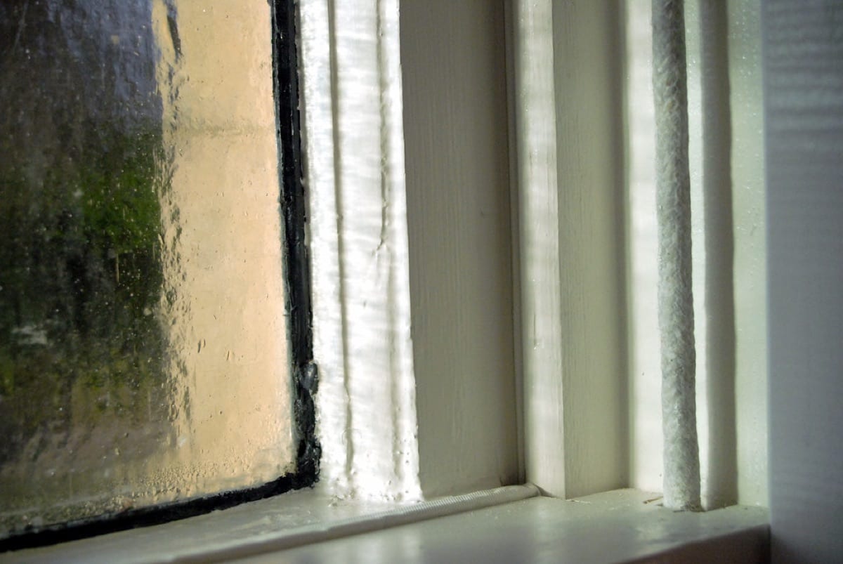 Condensation running down cold single-pane glass beside a painted sash and seal