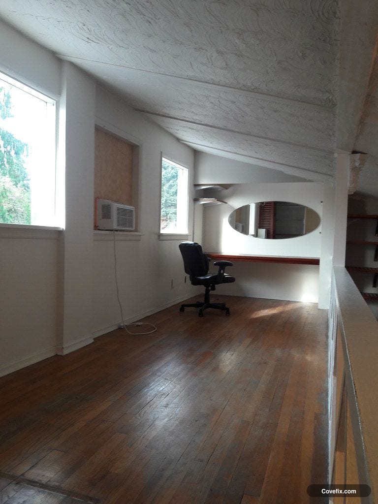 A window air conditioner installed in a plain upstairs room